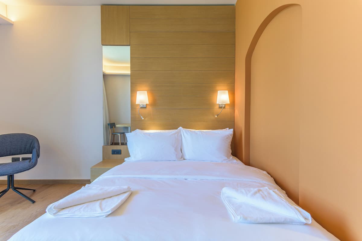 A hotel room with a bed, two bedside lamps, a chair, and a wooden headboard.