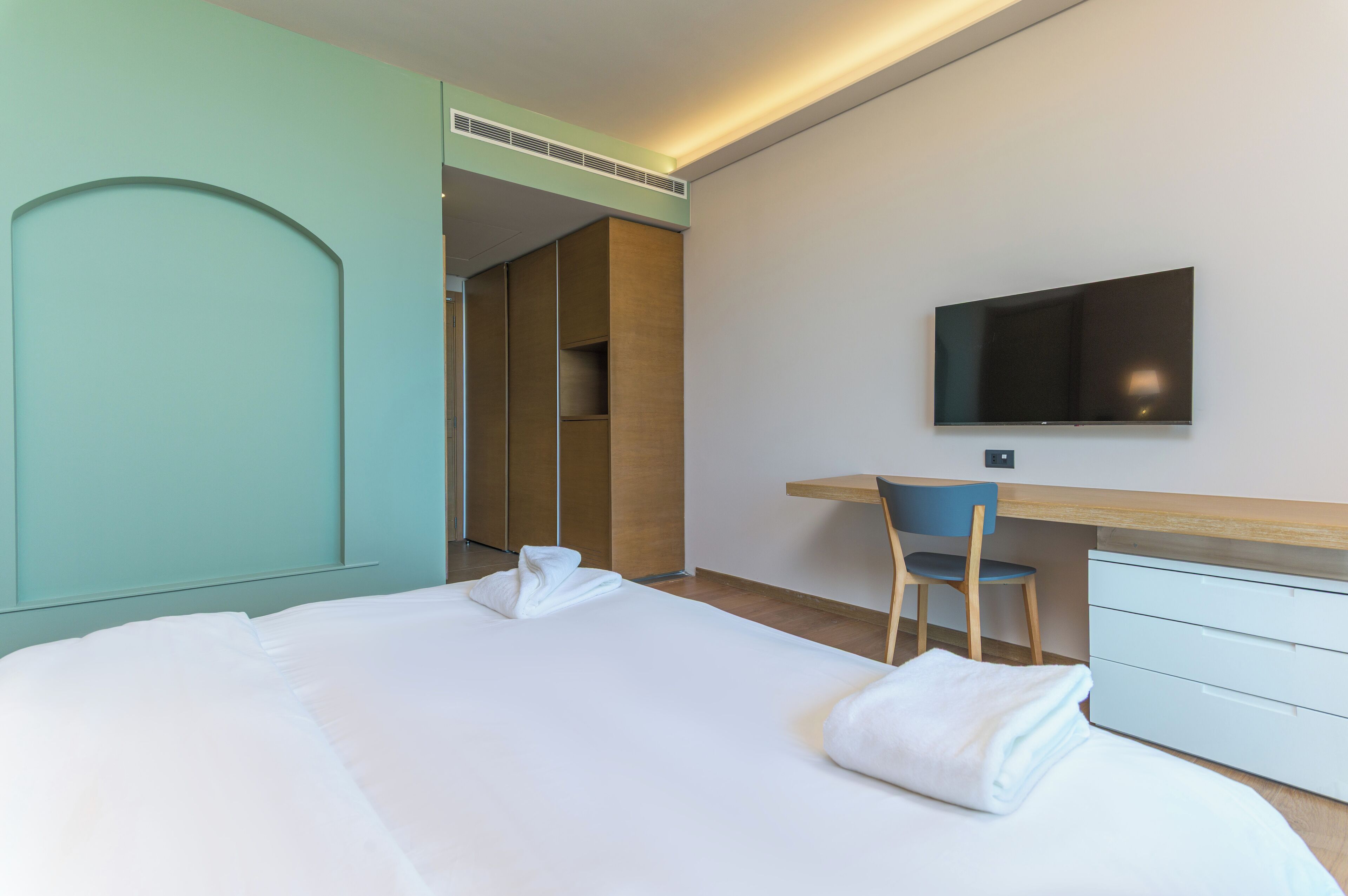 A hotel room with a bed, a desk, a chair, a TV, and a wardrobe.