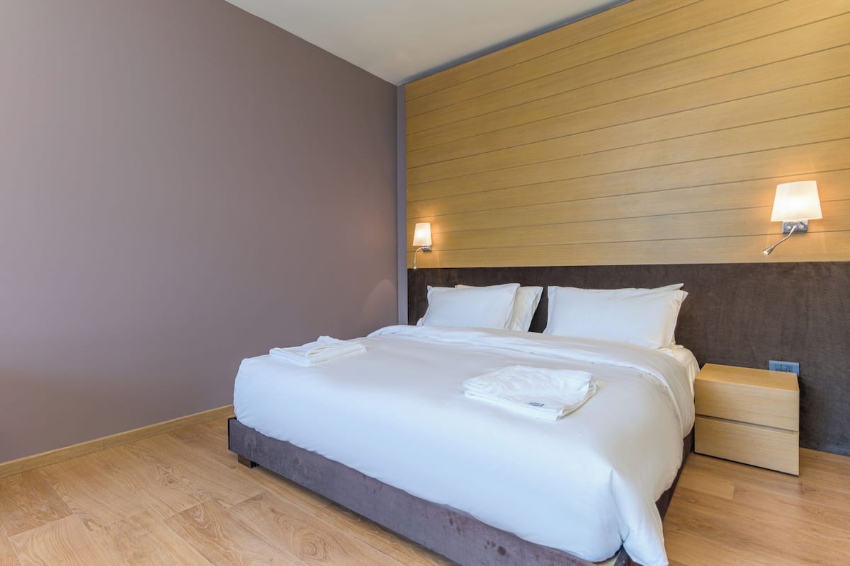 A neatly made bed with white linens, a wooden headboard, and two bedside tables with lamps.
