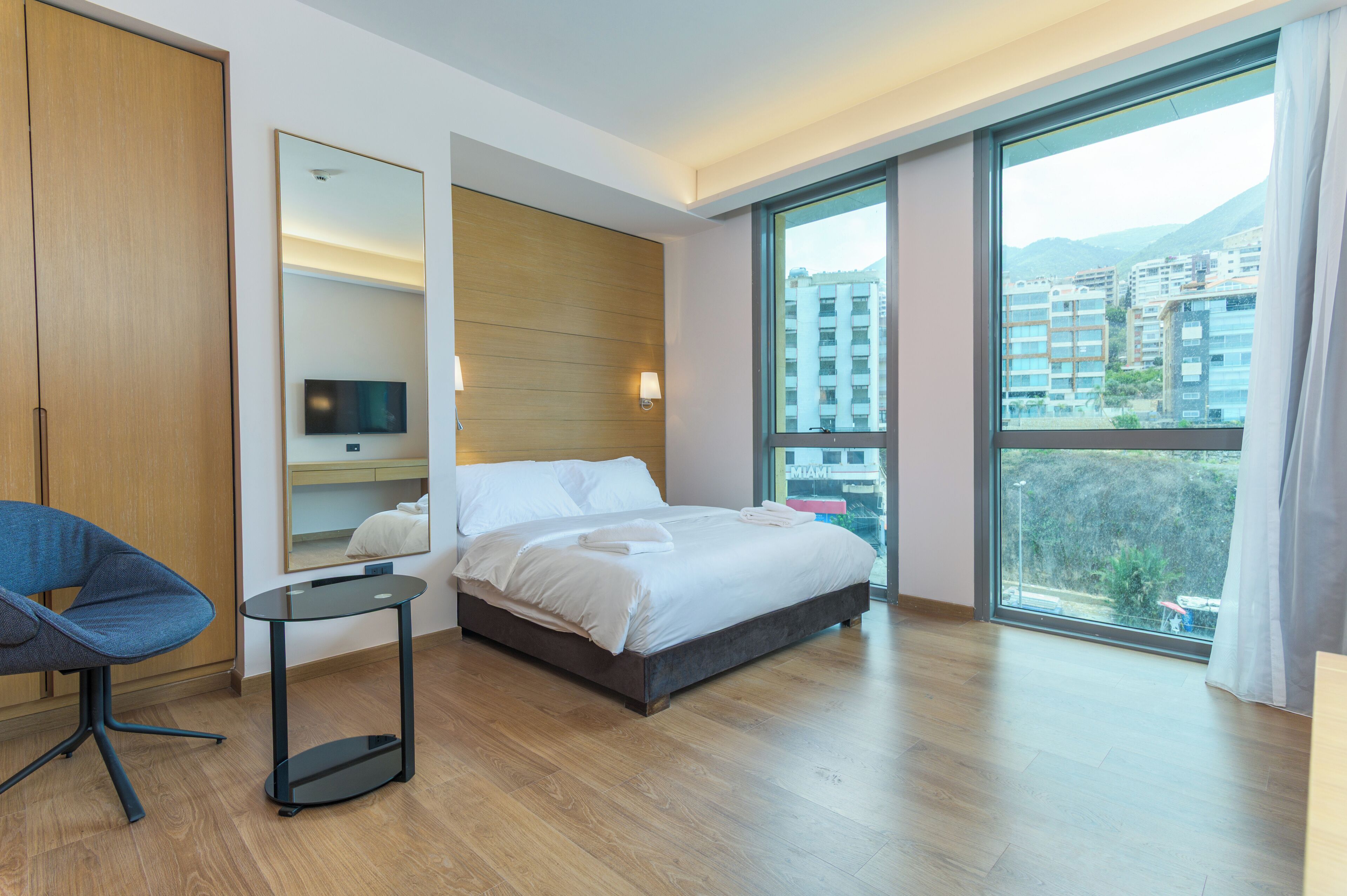 A modern hotel room with a large bed, a TV, a desk, and a view of the city.