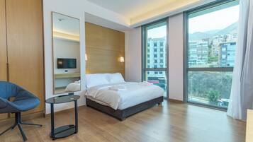 A modern hotel room with a large bed, a TV, a desk, and a view of the city.