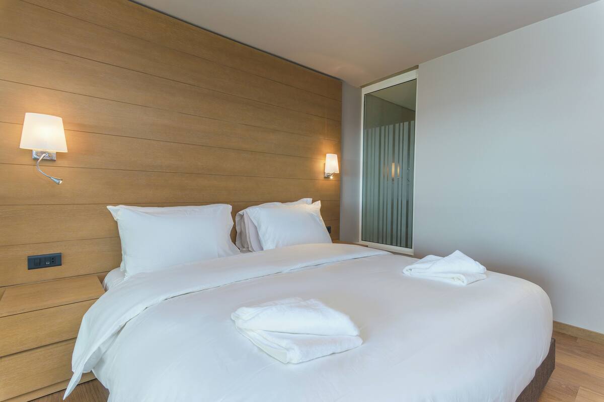 A neatly made bed with white linens and two wall-mounted lamps.