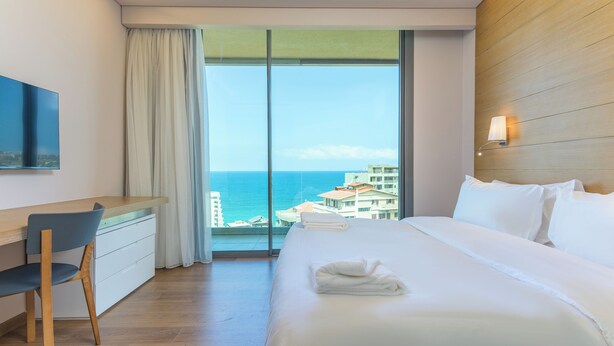A hotel room with a large bed, a desk, a chair, and a view of the ocean. - Jounieh Living - Residences by Local Host (Jounieh)