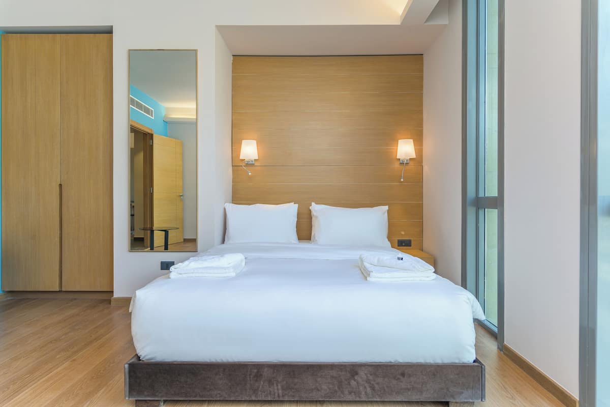 A hotel room with a large bed, wooden headboard, two bedside lamps, and a large mirror.