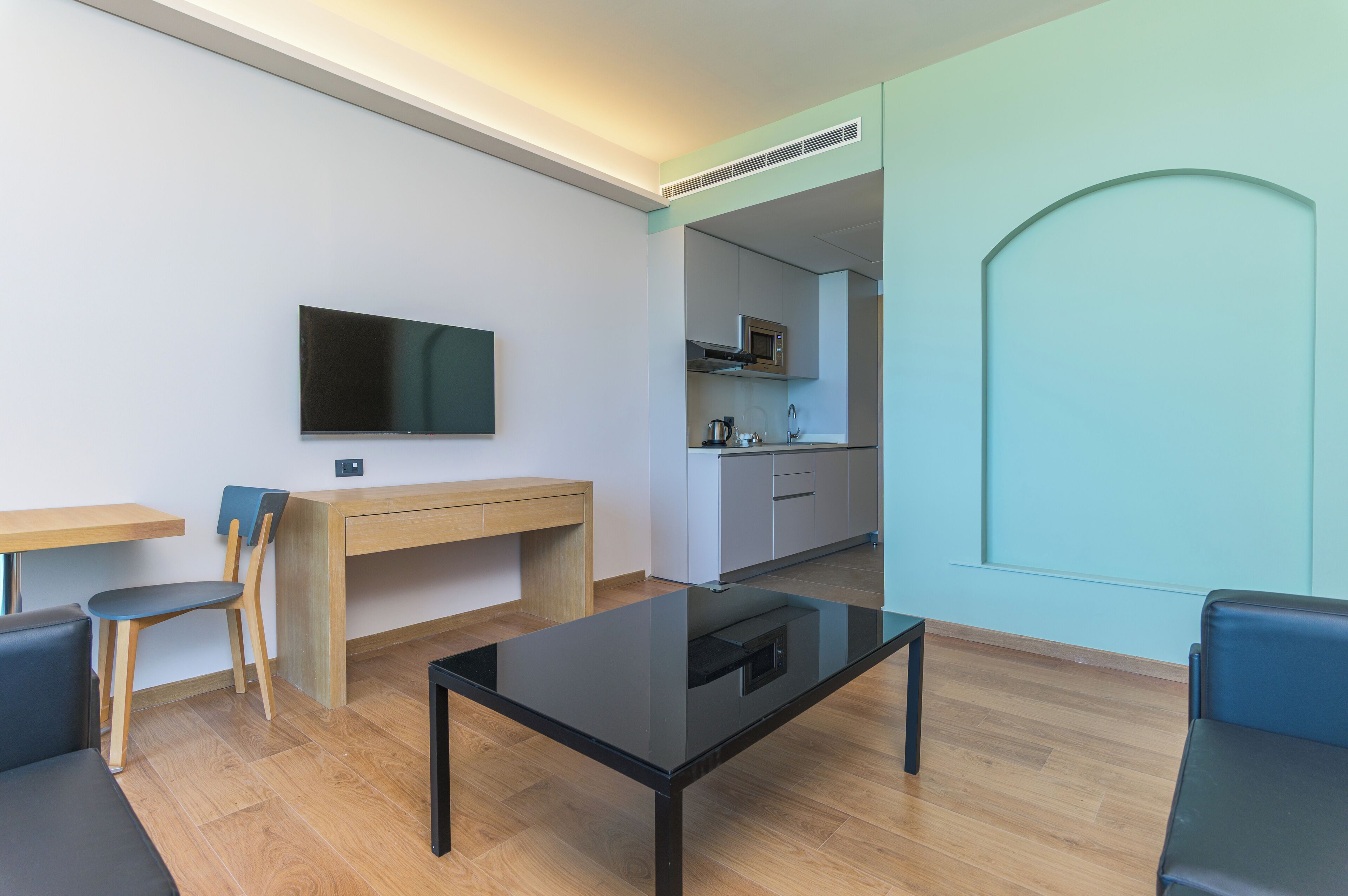 Een moderne woonkamer met een flatscreen televisie, een glazen salontafel en een eethoek met een houten bureau en stoelen.