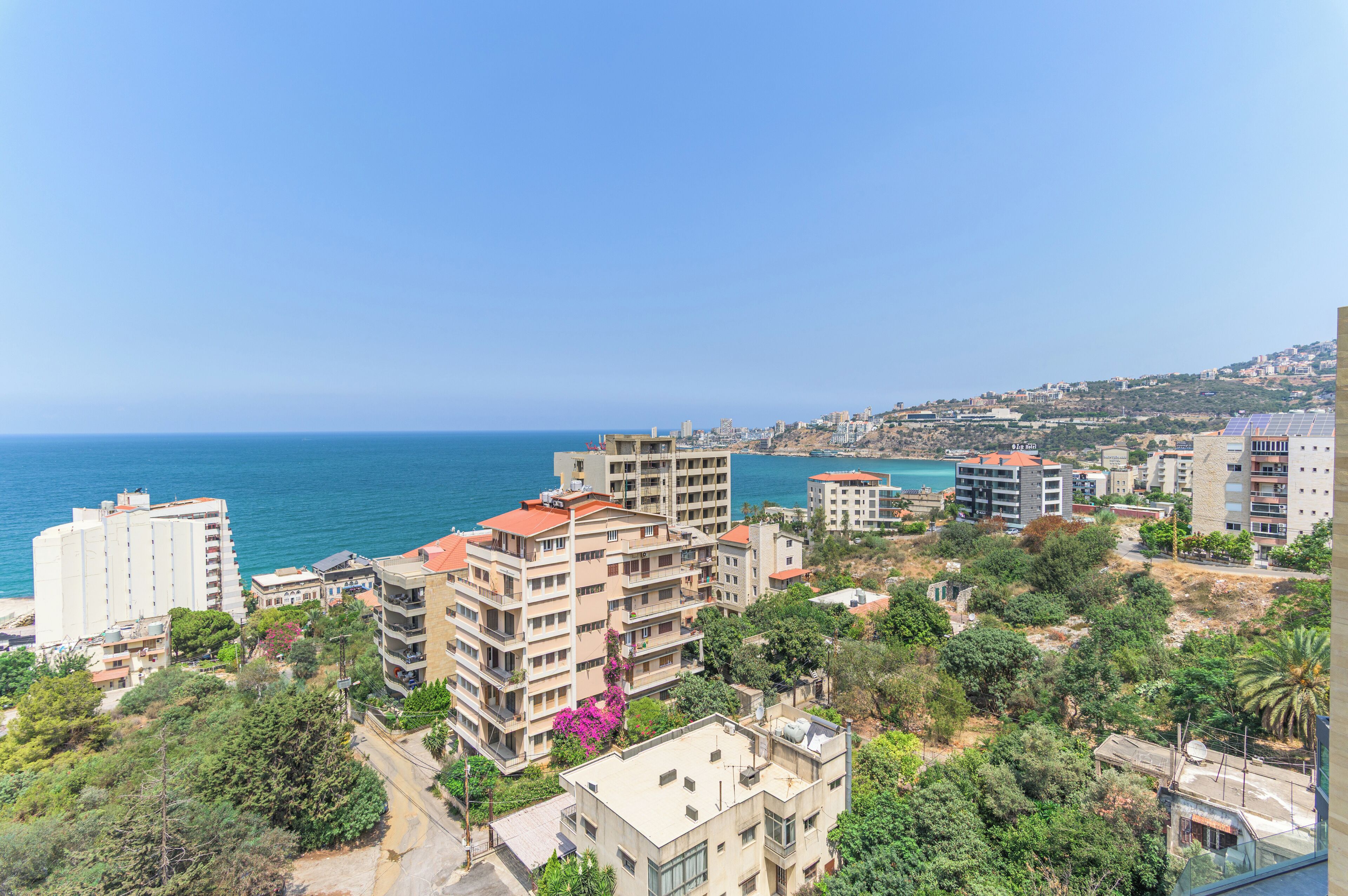 A coastal cityscape with high-rise buildings, a clear blue sky, and a view of the sea.