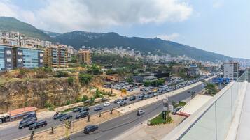 Uma rua urbana movimentada com edifícios, carros e montanhas ao fundo.