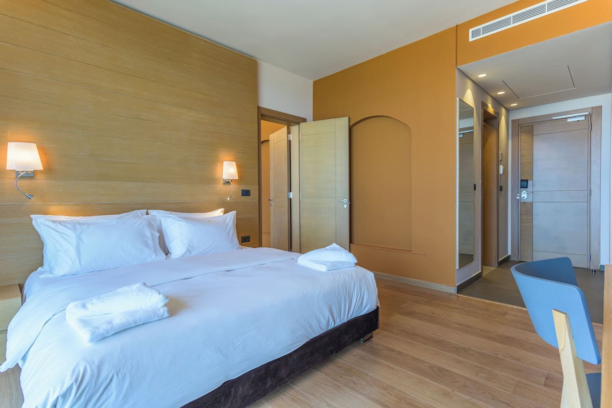 A hotel room with a large bed, bedside lamps, a wooden headboard, and a mirror.