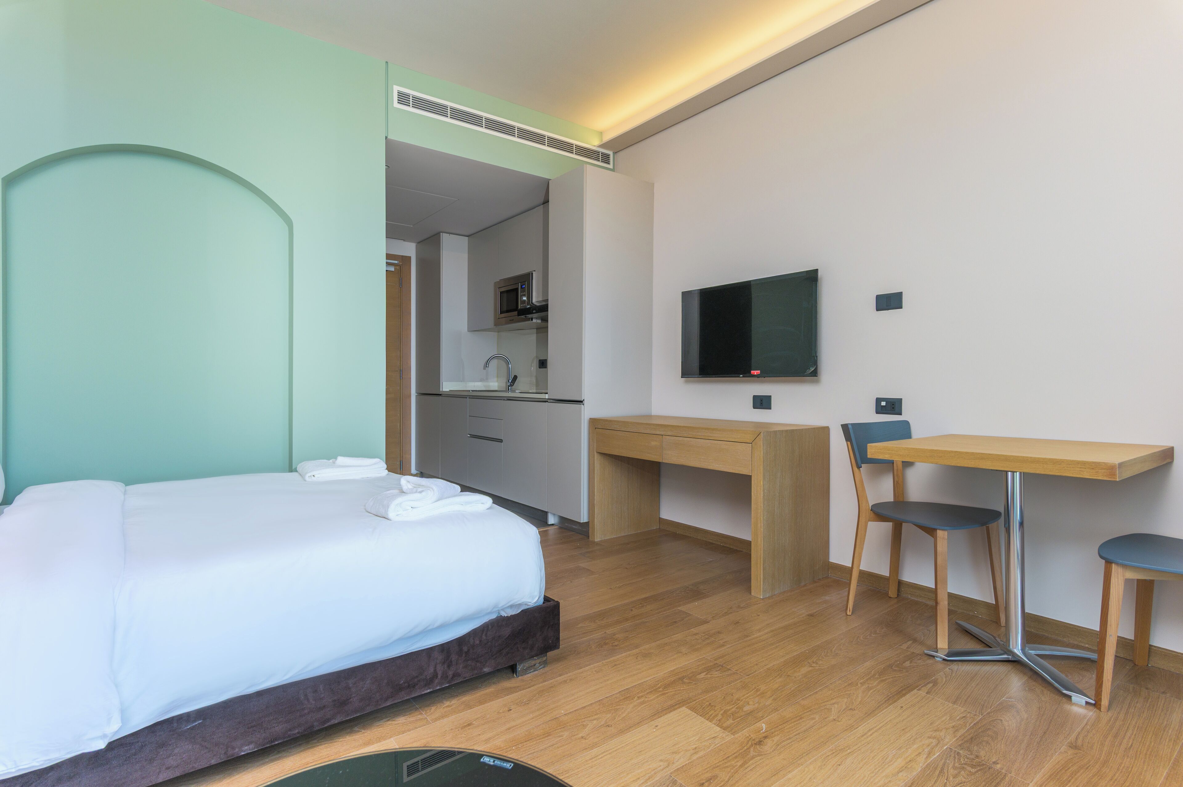 Ein Hotelzimmer mit Bett, Schreibtisch, Fernseher und einer Küchenzeile.