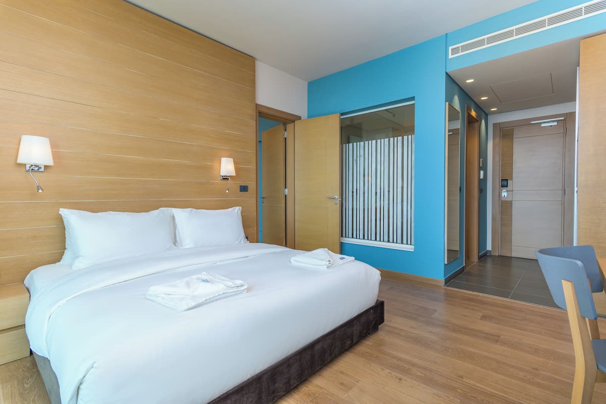 A modern hotel room with a large bed, wooden headboard, and a blue accent wall.