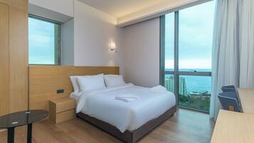 A modern hotel room with a large bed, a nightstand, a small table, and a view of the ocean.