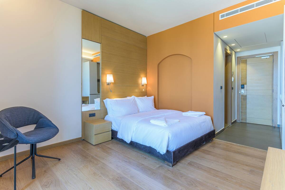 A modern hotel room with a bed, a chair, a nightstand, and a mirror.