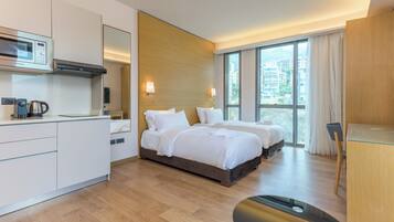 Una habitación de hotel moderna con kitchenette, dos camas, un ventanal con vistas y un escritorio.