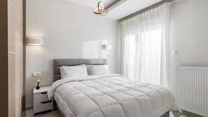 A modern bedroom with a bed, bedside tables, a nightstand, a wall-mounted light, and a window with sheer curtains. - Eleanor by halu! (Thessaloniki)