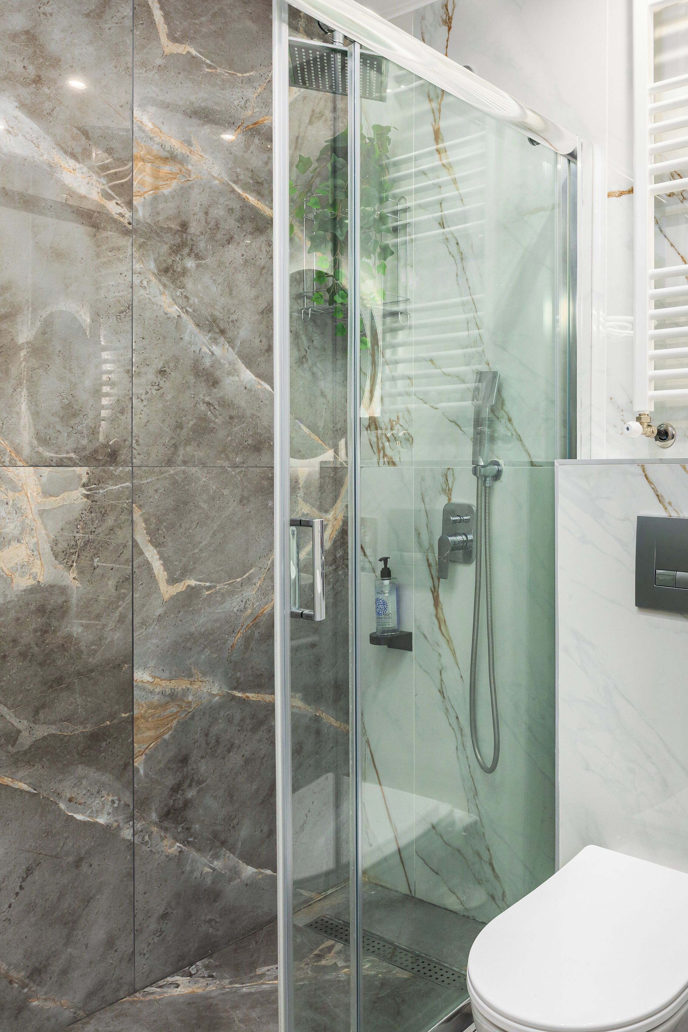 Een moderne badkamer met een douche in glazen cabine, marmeren tegels en een wit toilet.