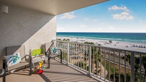 A balcony with a view of the beach, a chair, a small table, and a colorful bucket. - 5th Floor Perfect Location at The Summit w/Beach Chairs Included! (Panama City Beach)