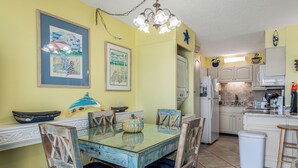 A dining area with a glass table, wooden chairs, and a kitchen in the background. - 5th Floor Perfect Location at The Summit w/Beach Chairs Included! (Panama City Beach)