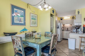 A dining area with a glass table, wooden chairs, and a kitchen in the background.