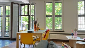 A bright room with large windows, a dining table with yellow chairs, and a sofa. - Bright loft in the heart of Paris (Liège)
