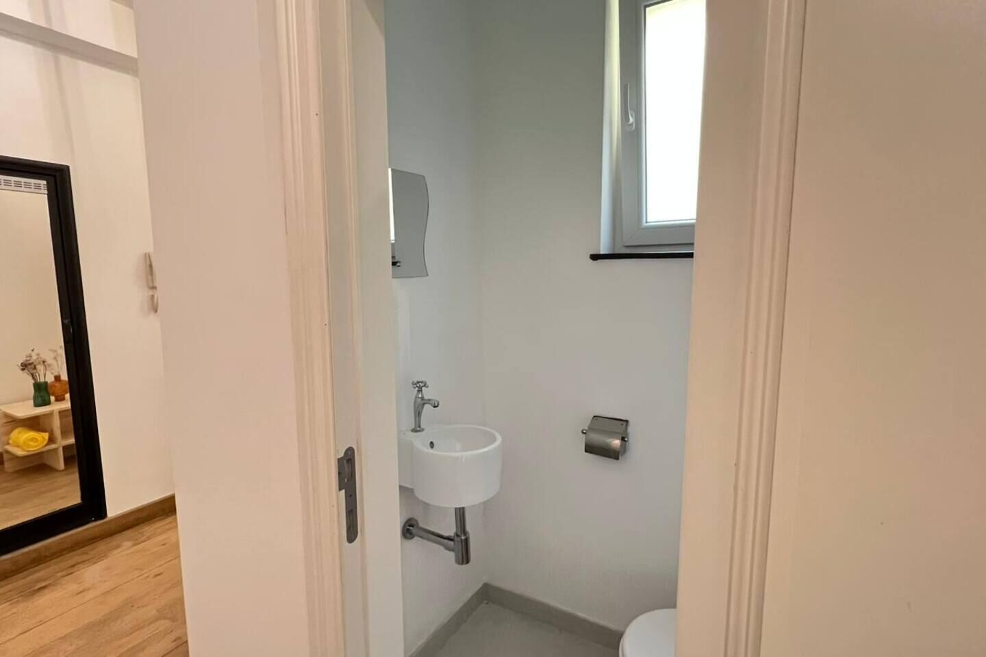Een kleine, schone badkamer met een wit wastafel, toilet en raam.