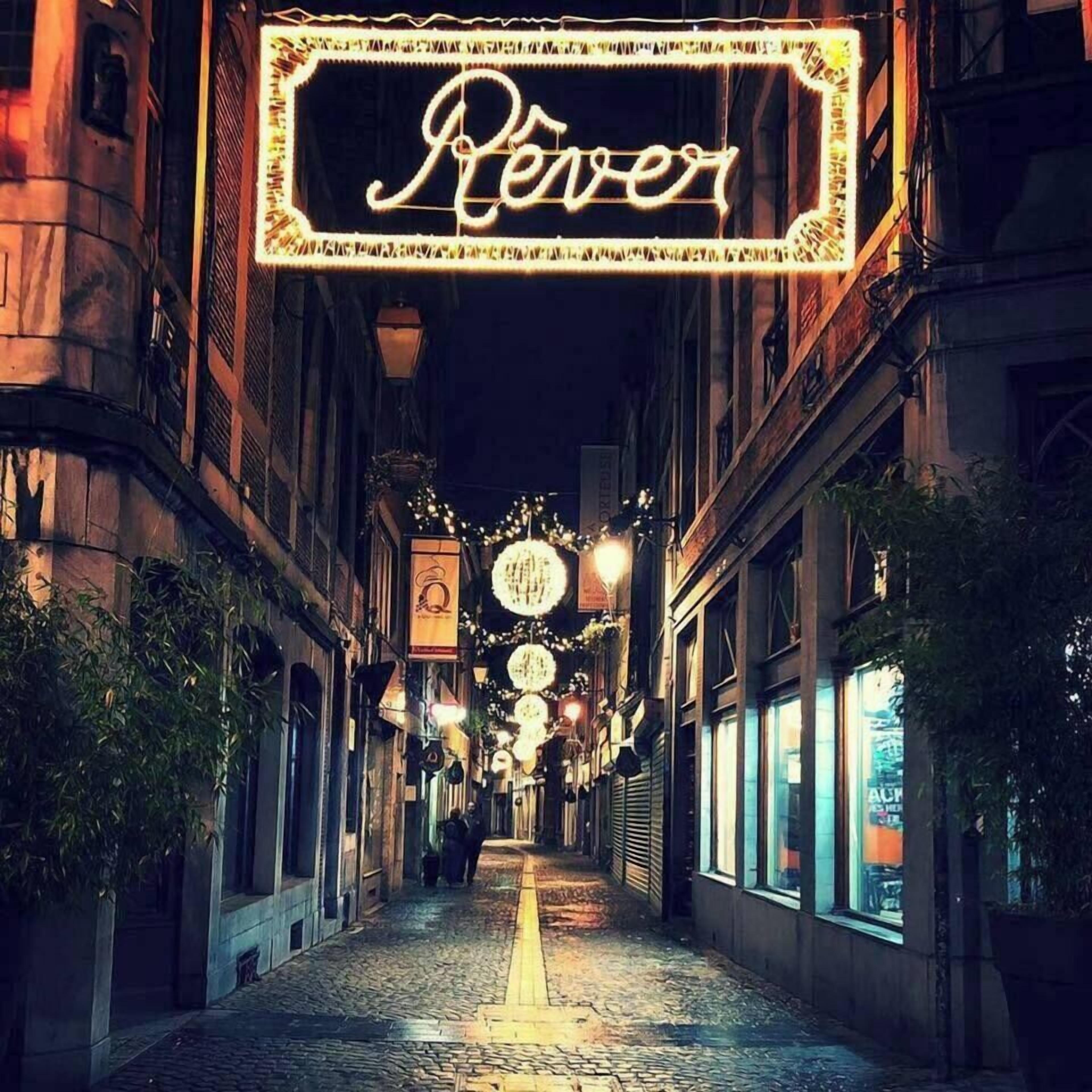 Een smalle straat met kinders hoofdverharding, verlichte borden en hangende lampen, wat wijst op een historische of toeristische omgeving.