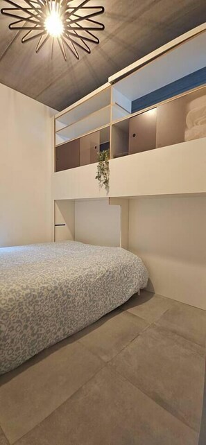 Ein modernes Schlafzimmer mit Etagenbett, Deckenleuchte und einer Pflanze auf dem oberen Bett.