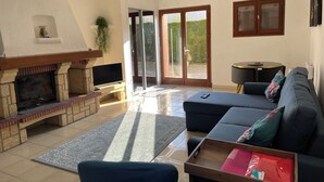 Un salon avec une cheminée, un canapé, un téléviseur et une porte-fenêtre coulissante donnant sur un jardin.