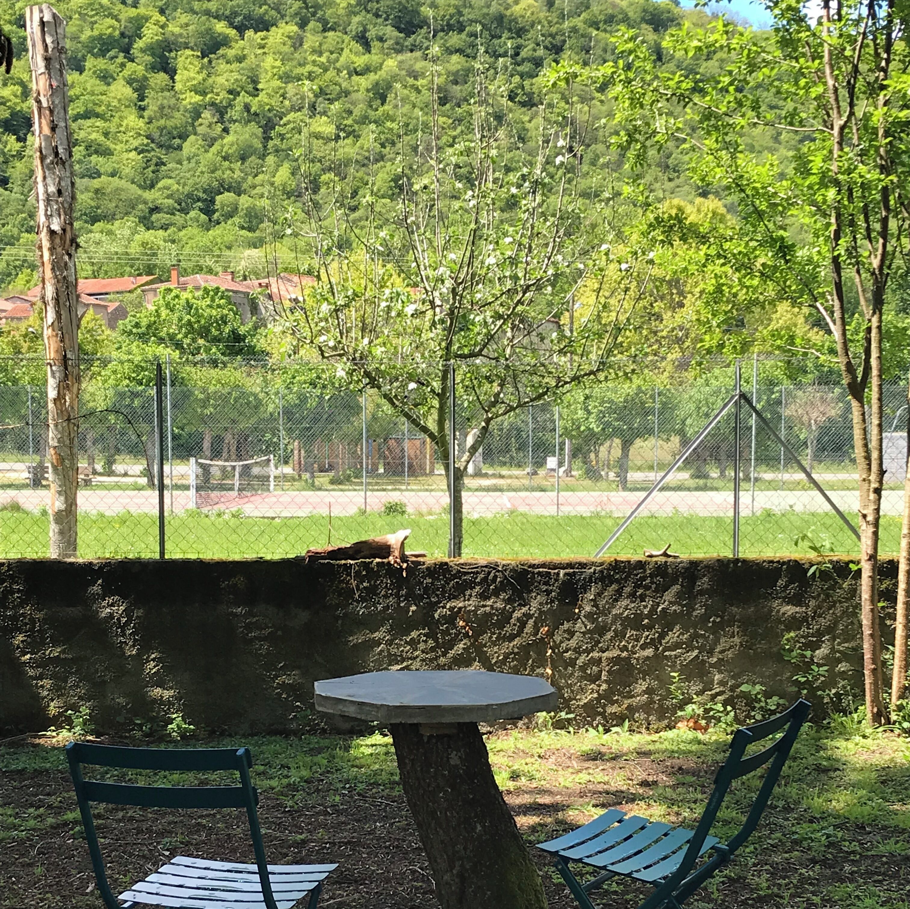 A park with a table and chairs, surrounded by a fence and trees.