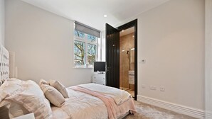 A bedroom with a bed, a TV, a window, and a bathroom door. - Brampton Grove Cozy Apartment - London (London)