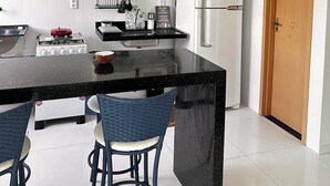 A modern kitchen with white cabinets, a black countertop, a microwave, a refrigerator, and a wooden door. - Apartment with river view (Barreirinhas)