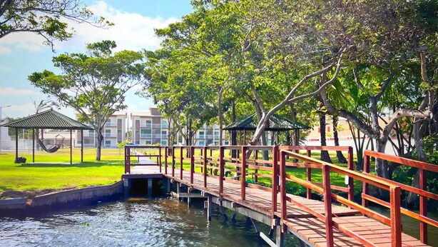 A wooden bridge over a water body with a grassy area and trees in the background. - Apartment with river view (Barreirinhas)
