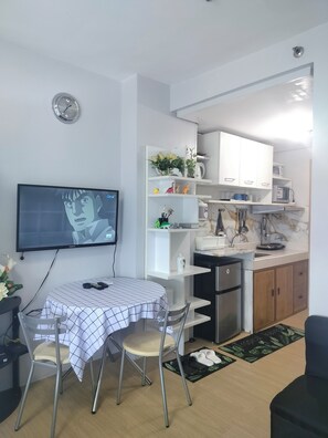 Une cuisine moderne avec des meubles blancs, un four à micro-ondes et un évier. On y trouve également un coin repas avec une table et des chaises, ainsi qu’un téléviseur fixé au mur.
