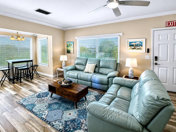 A living room with a sectional sofa, a coffee table, a dining table with chairs, and a ceiling fan.