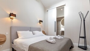 A modern hotel room with a large bed, two wall-mounted lights, a wooden side table, and a floor lamp.