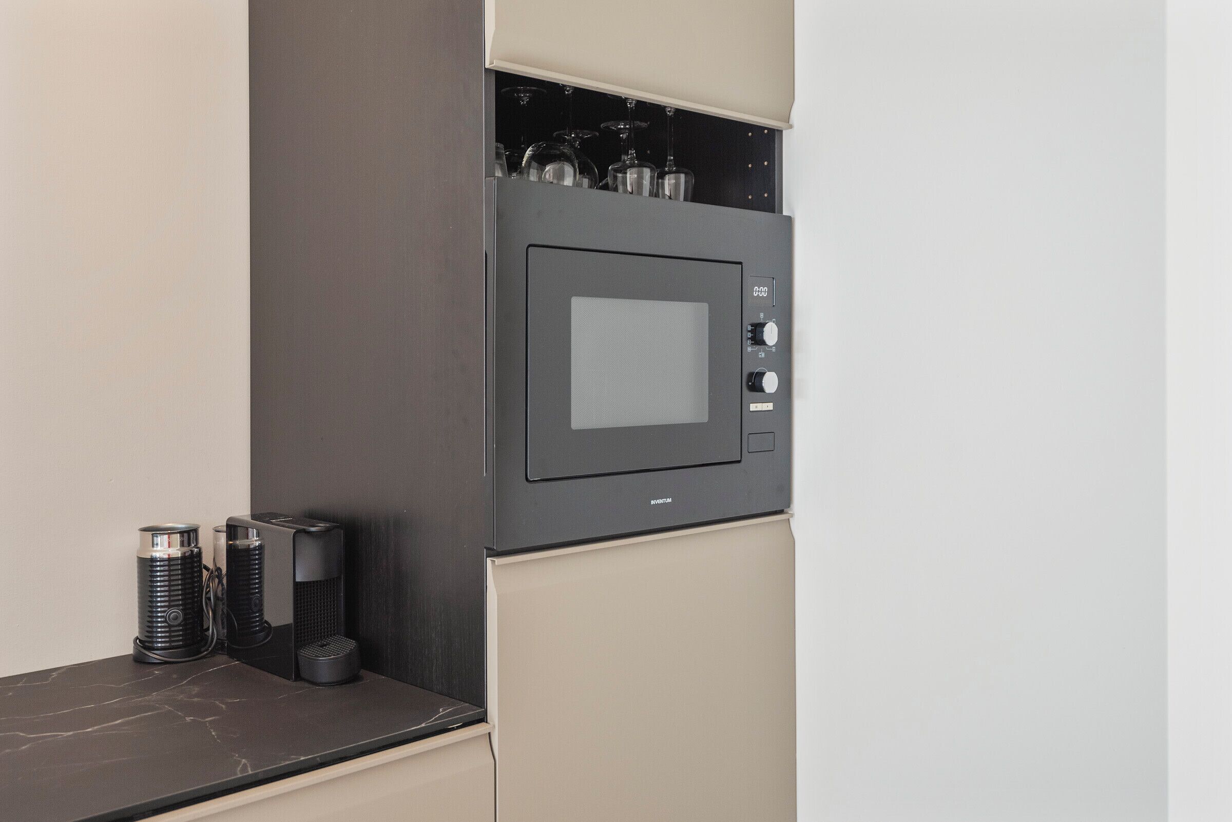 Une cuisine équipée d’un four à micro-ondes encastré, d’une machine à café et d’un porte-verres à vin.
