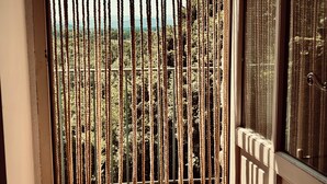 Ein Zimmer mit Blick durch ein Fenster mit vertikalen Rollläden, einem Fliesenboden und einer Tür mit einem Metallgitter.