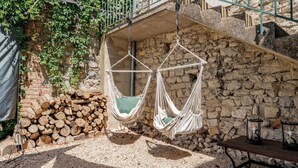 Zwei weiße Hängematten an einer Steinmauer, ein Holzstoß und ein Tisch mit Laternen.