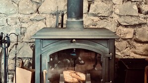 Eine Steinsäule, ein schwarzer Kaminofen mit Glastür und ein gefliester Boden.