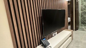 A modern living room with a flat-screen TV mounted on a wooden wall, a built-in soundbar, and a wooden console table. - 205 Al-najeh JRE Apartments For Rent ave (Amman)