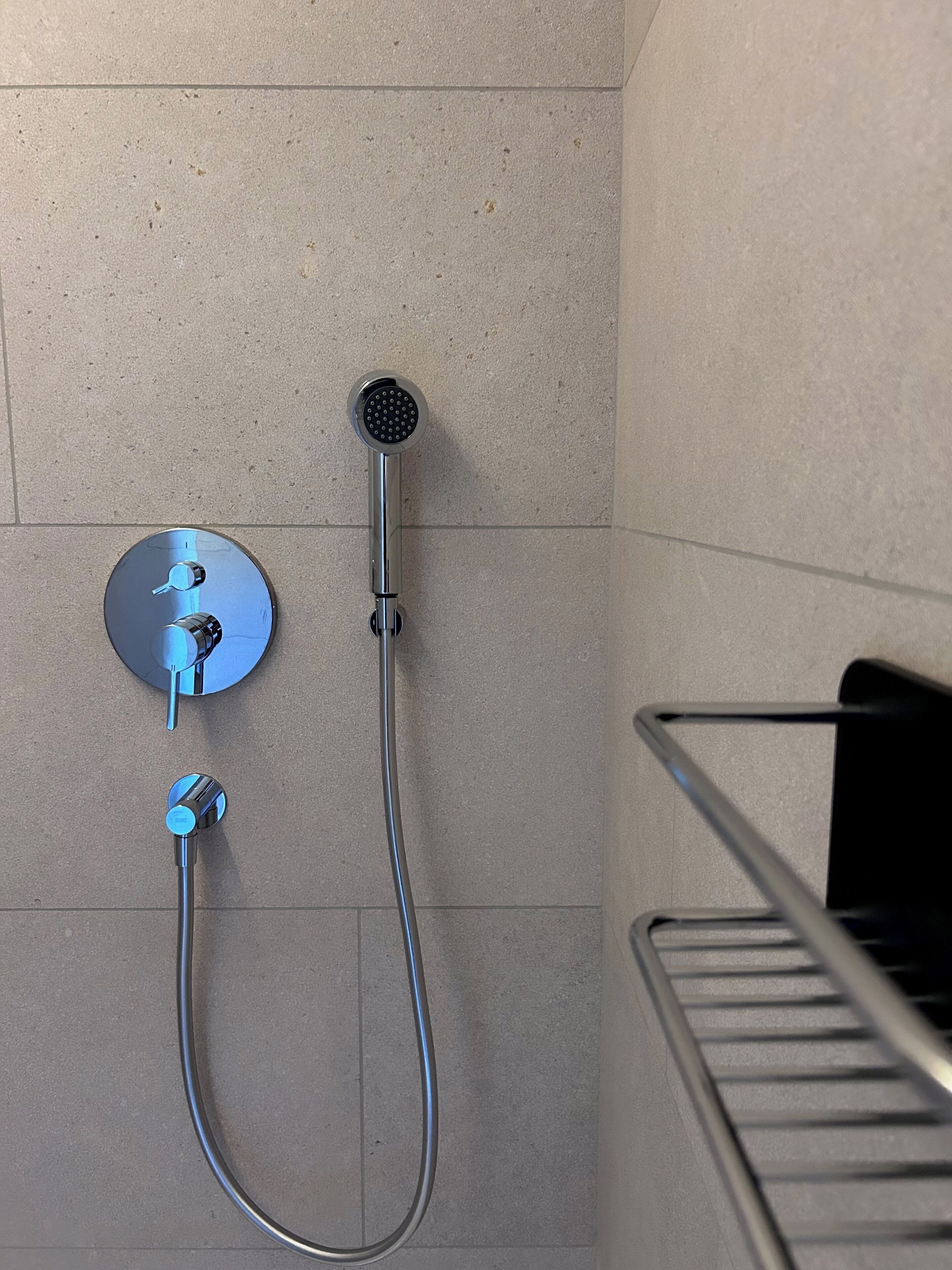 A shower with a handheld showerhead and a wall-mounted control.