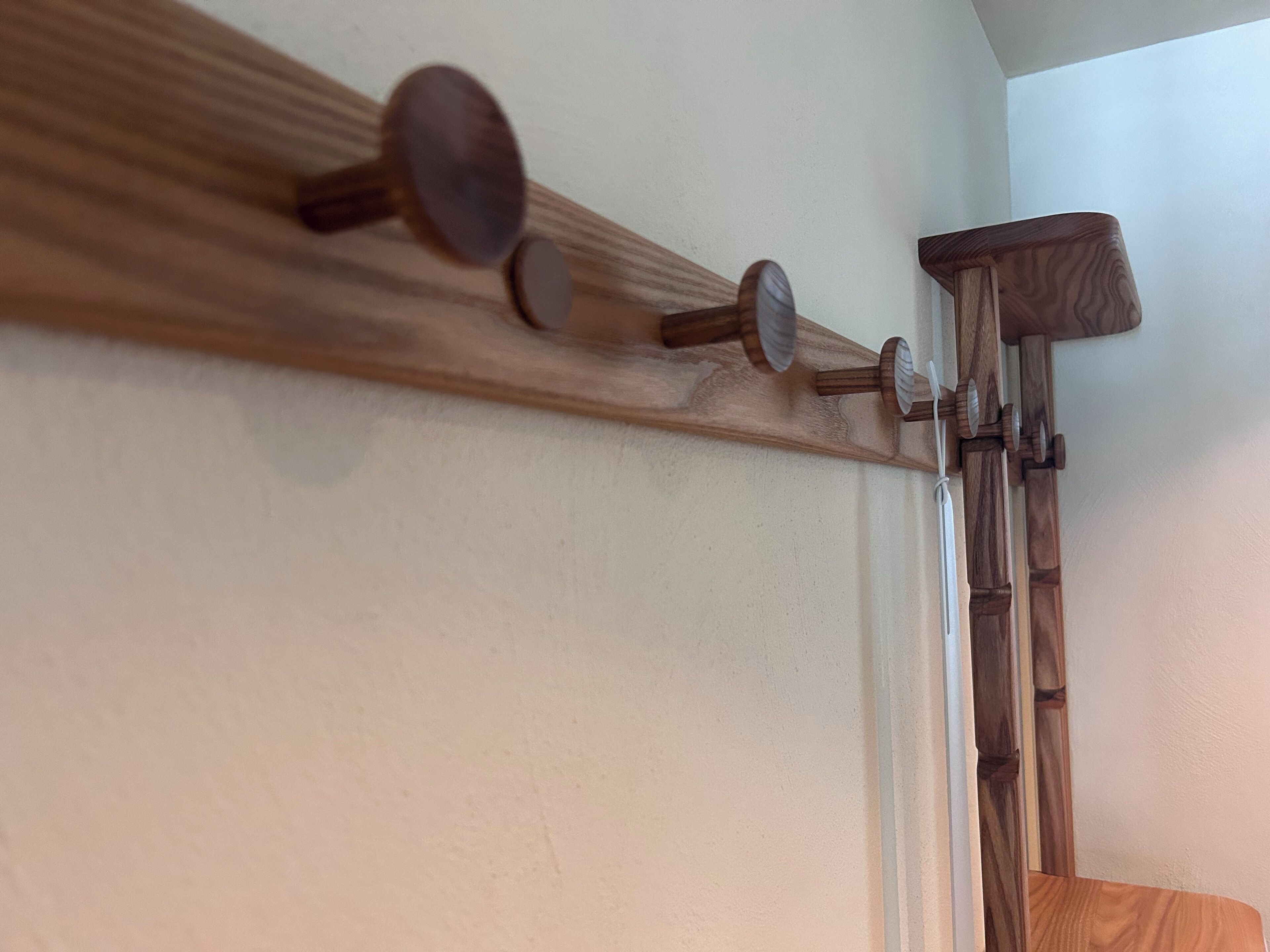 Ein hölzerner Kofferständer mit drei Haken an einer weißen Wand.