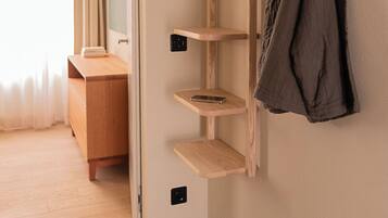 Habitación de hotel con un estante de madera, un perchero y un par de zapatillas deportivas sobre un felpudo.