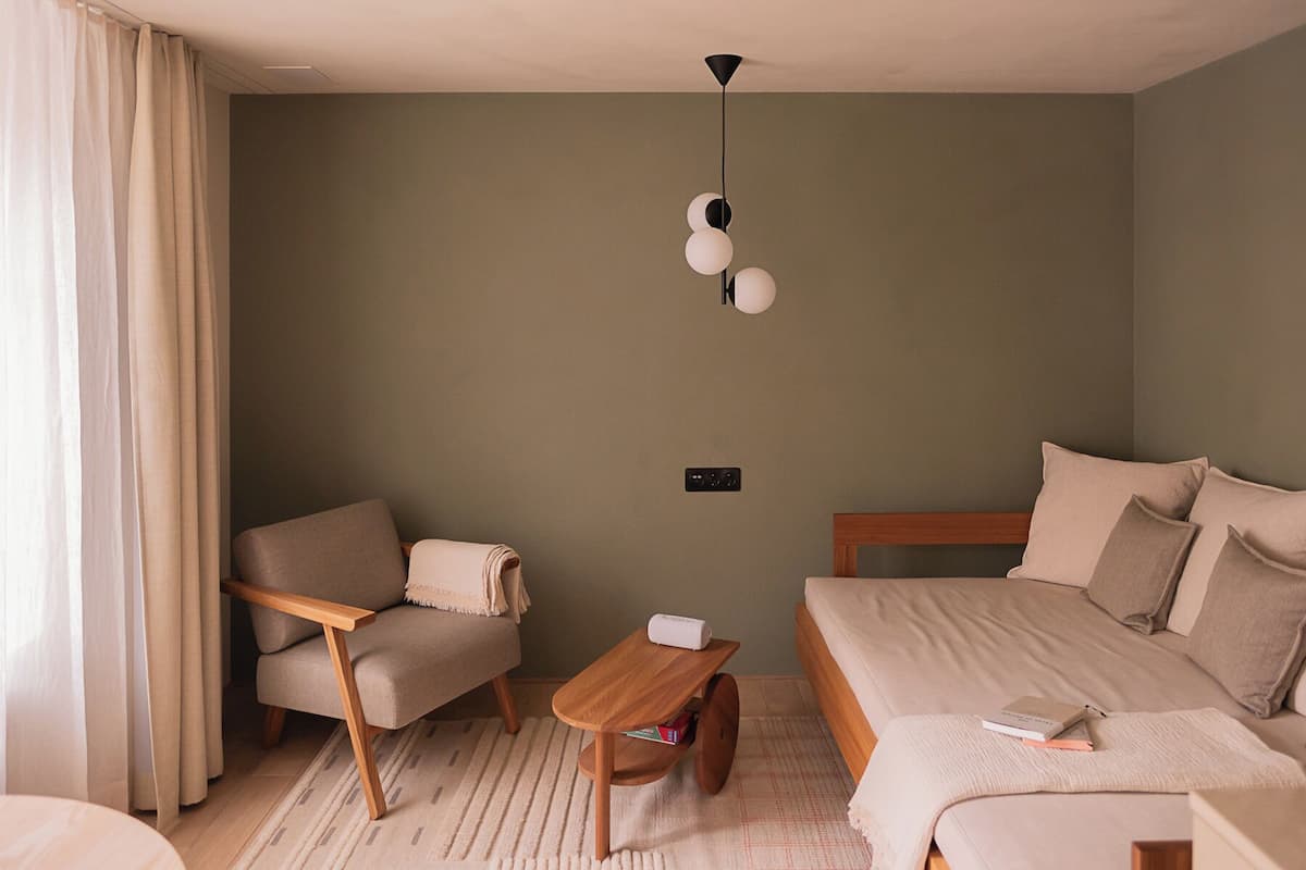 A modern bedroom with a bed, a chair, a small wooden table, and a ceiling light fixture.