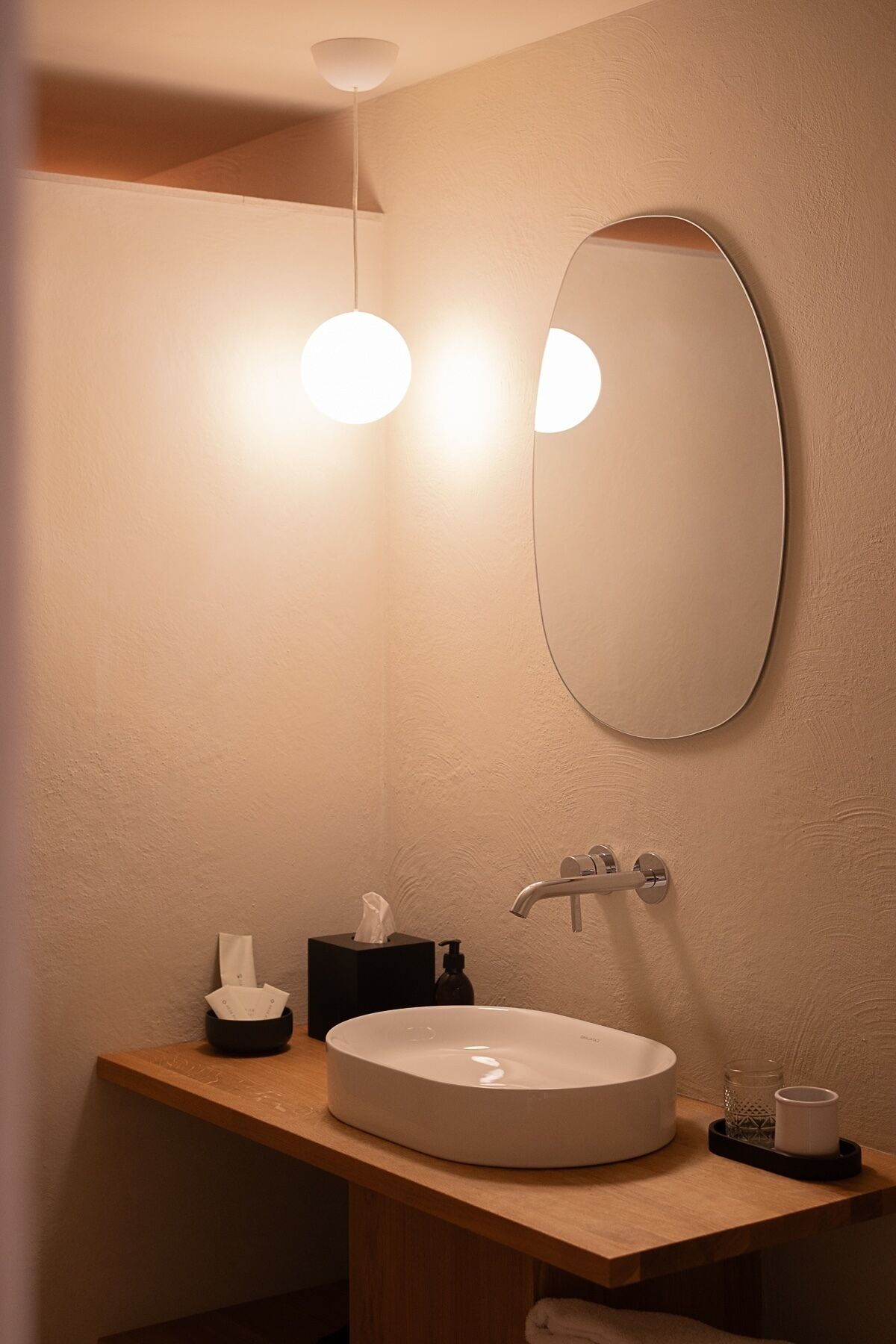 Un baño con un lavabo redondo, un espejo, una toalla, dispensador de jabón y una caja de pañuelos.