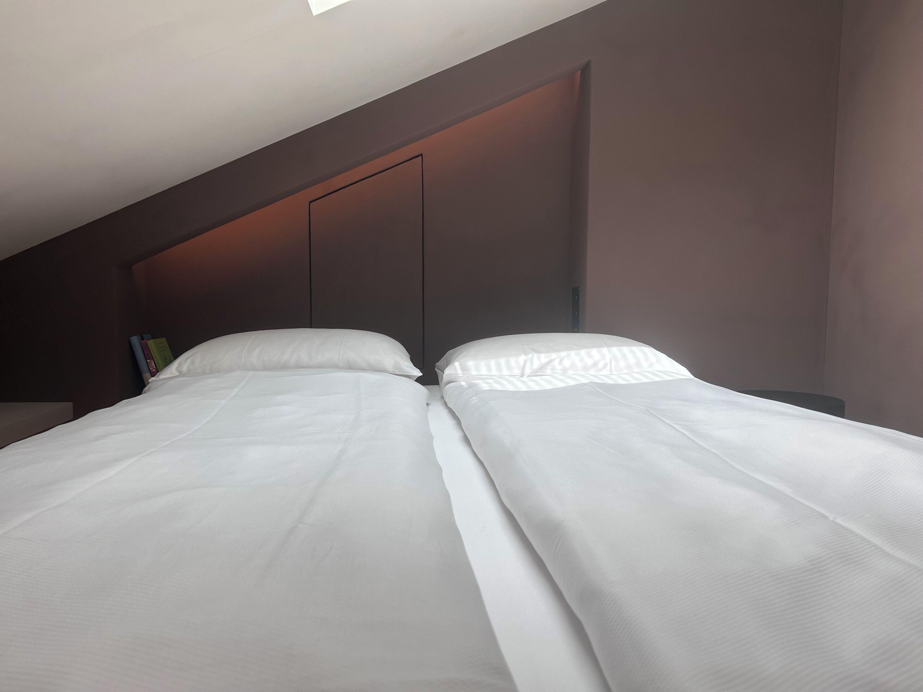 Habitación de hotel moderna con una cama grande, cabecera oscura y una mesita de noche pequeña con libros.