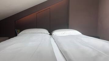 Habitación de hotel moderna con una cama grande, cabecera oscura y una mesita de noche pequeña con libros.