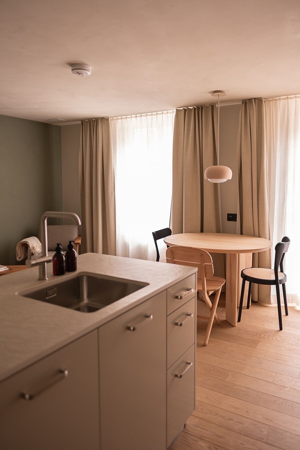 A compact kitchen with a sink, a dining table with chairs, and a pendant light.