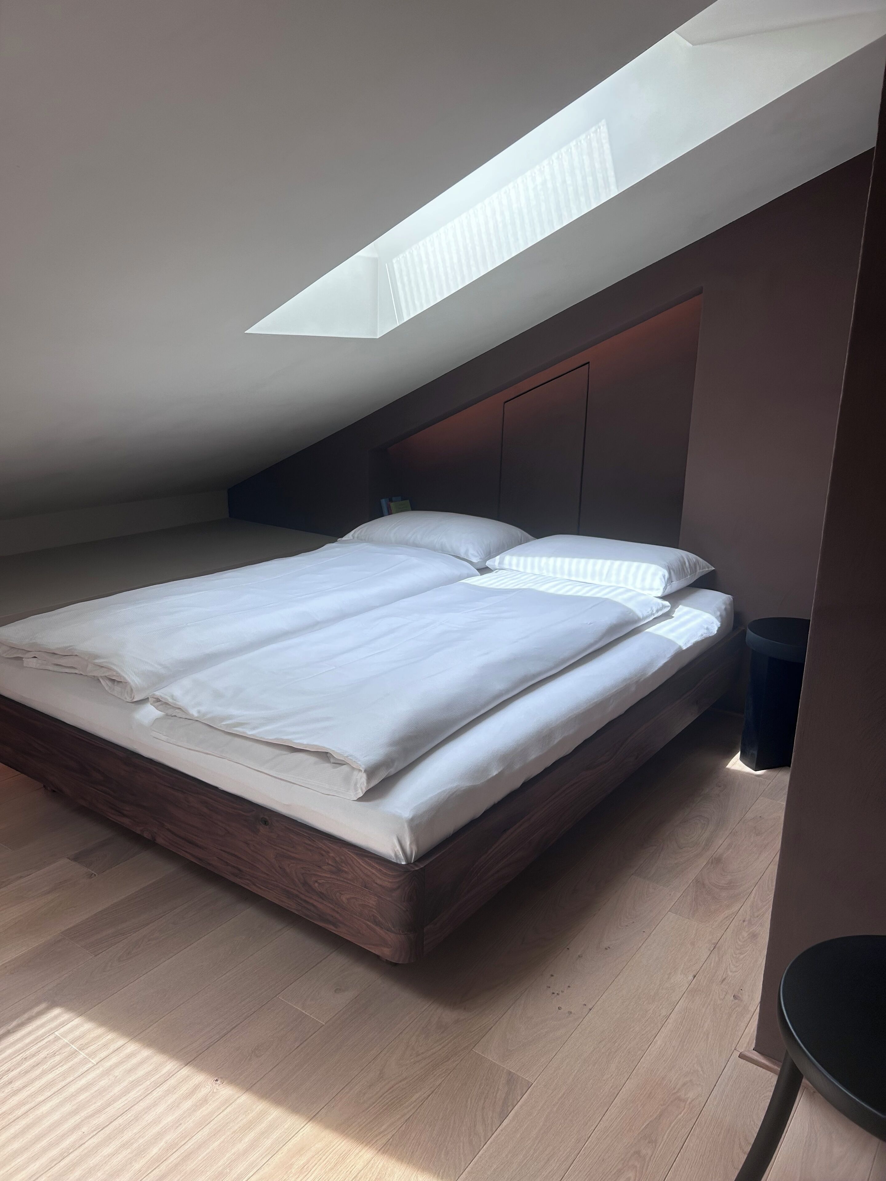 A modern bedroom with a skylight, wooden flooring, and a bed with white linens.