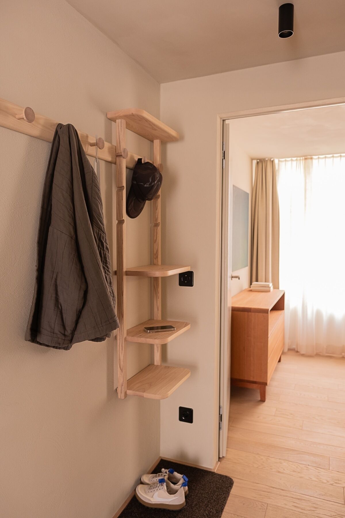 Una habitación con perchero de madera, estantes, un espejo y una puerta que da a otra estancia.