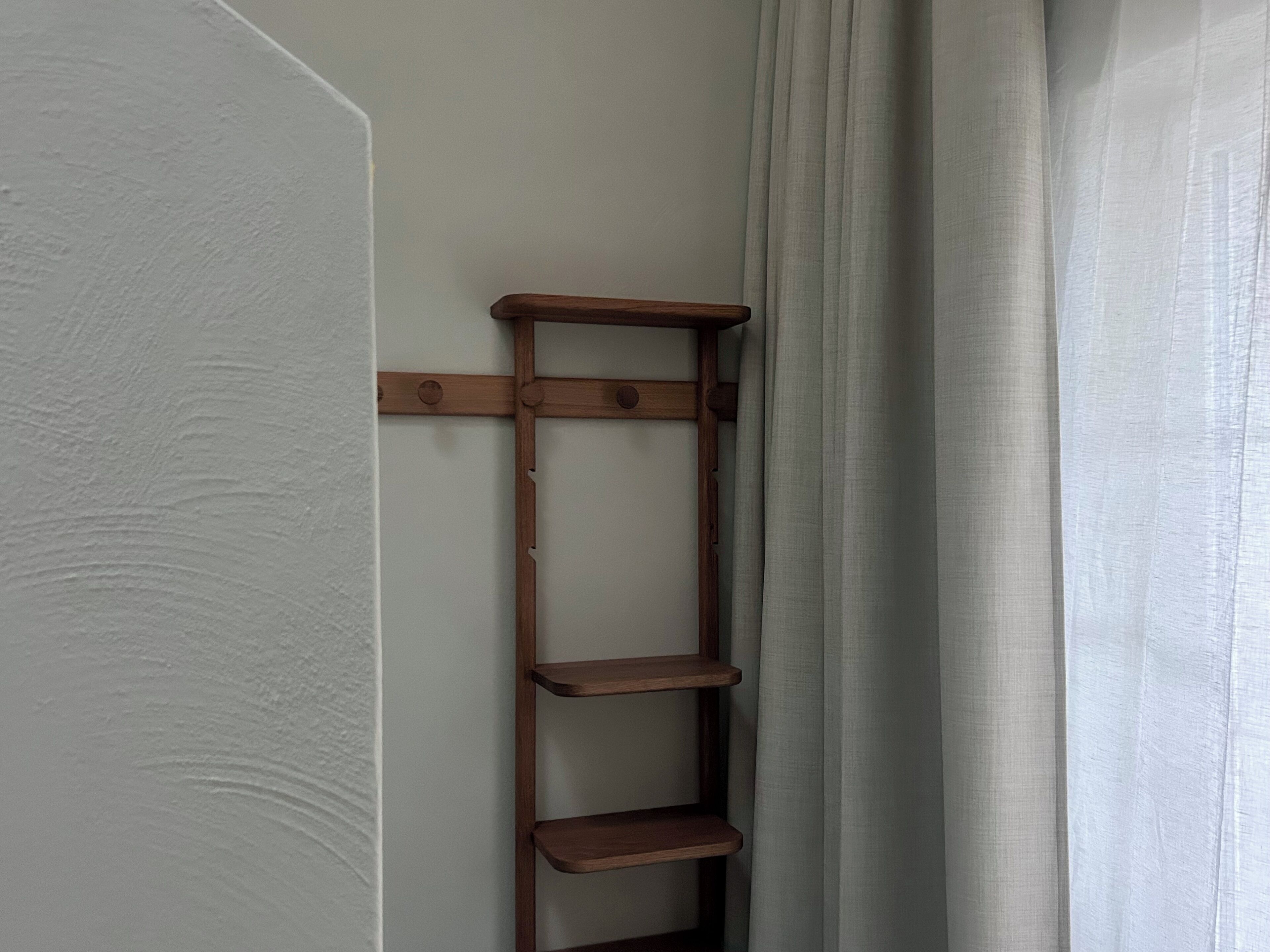 Une étagère en forme d’échelle en bois, adossée à un mur, avec une porte blanche et un rideau.